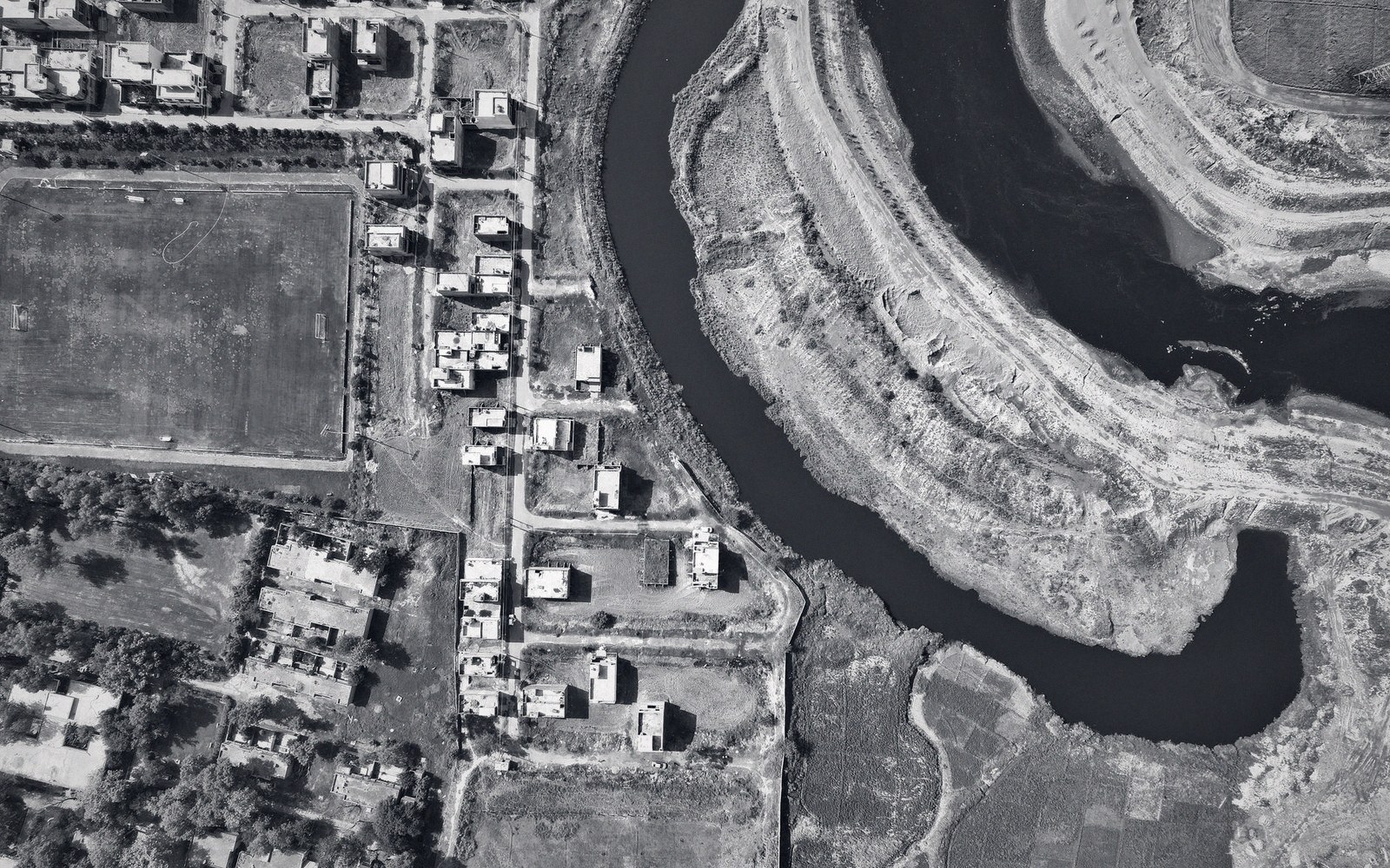 A vertical aerial photograph of a meander loop passing through a town, black and white