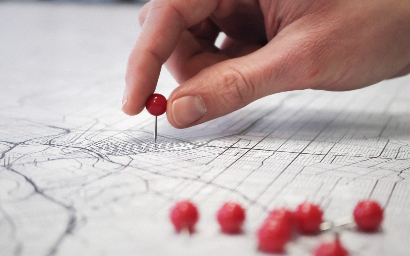 A hand placing a red pin on a printed plan, a row of pins already set along a line